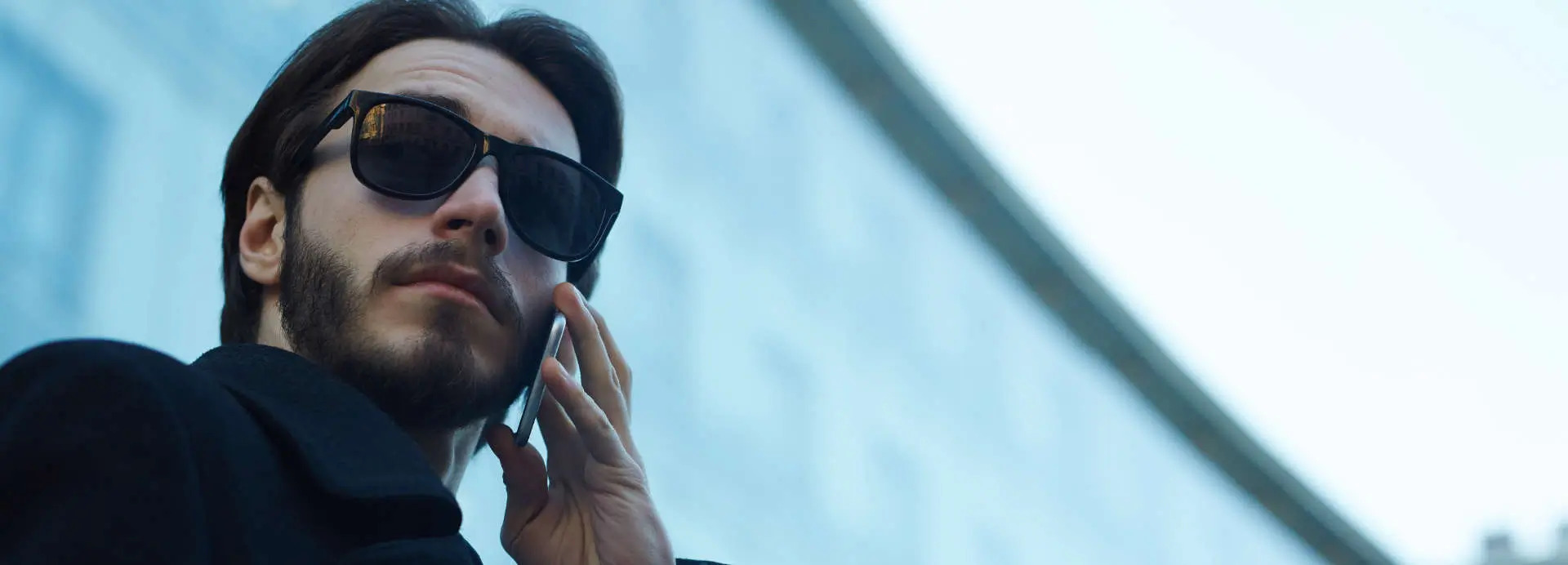  World Wide private investigator in front of a building using a phone while observing the area through dark sunglasses